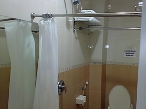 Un baño con cortina de ducha, toallero, inodoro y un cartel en la pared.