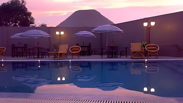 Une piscine entourée de chaises longues et de parasols, délimitée par un petit muret et avec une montagne en toile de fond.