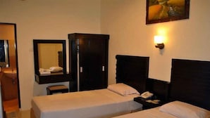 Une chambre d’hôtel avec deux lits simples, une armoire, une table de chevet avec une lampe et un miroir au mur.