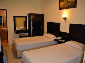Habitación de hotel con dos camas individuales, un armario, una mesita de noche con lámpara y un espejo en la pared.