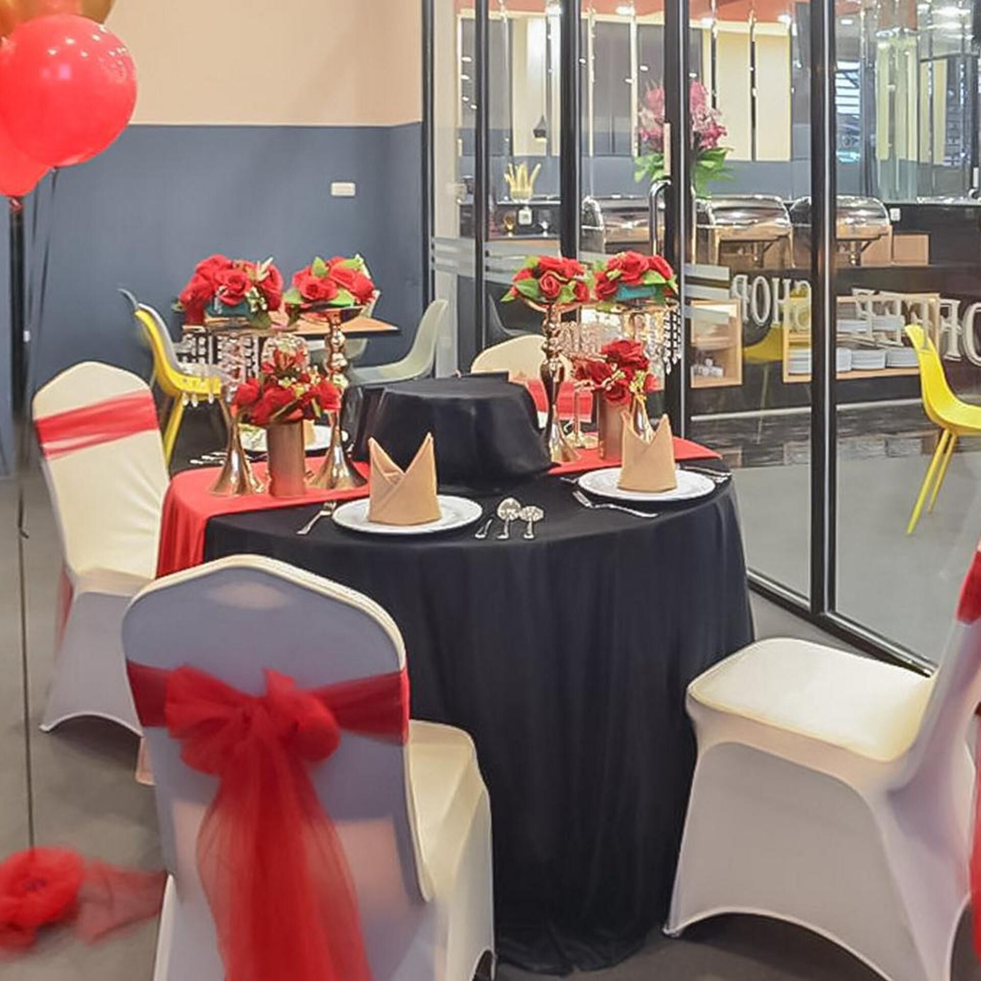A conference room with tables set for a meeting, decorated with red flowers and white chairs.