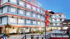 Un hotel de varios pisos con señalización llamativa, un área de estacionamiento y una acera para peatones.