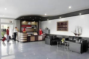 A hotel reception area with a reception desk, a clock, and a framed artwork on the wall.