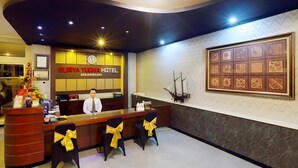 Una recepción de hotel con un reloj, un mapa enmarcado y un modelo de barco.