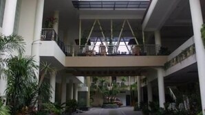 A multi-level atrium with a central staircase, surrounded by potted plants and columns. - Grand Mansion Hotel (Blitar)