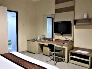 Une chambre d’hôtel comprenant un lit, un bureau avec une chaise, une télévision et une petite étagère.