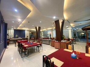 A spacious dining area with multiple tables and chairs, a central bar, and a view of the outdoors. - Grand Mansion Hotel (Blitar)
