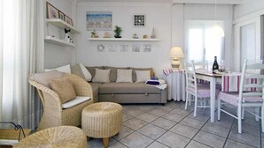 A cozy living room with a sofa, chairs, a dining table, and a small kitchen area. - MARICEL Apartment - right on the beach (Calafell)