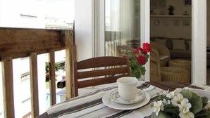 Een balkon met een eettafel, een houten stoel en een vaas met bloemen.