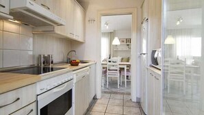 A modern kitchen with white cabinetry, a built-in oven, and a sink. There is a dining area visible through an open doorway. - MARICEL Apartment - right on the beach (Calafell)