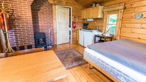 A cozy cabin with a brick fireplace, wooden walls, a dining table, a bed, and a small kitchenette. - Vacation home Elfvik by Interhome (Porvoo)
