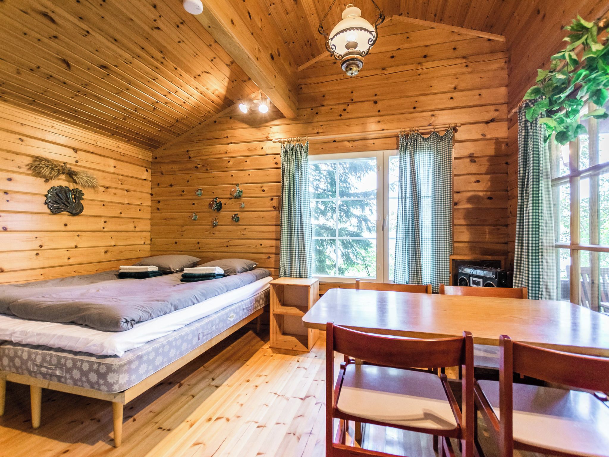 A wooden cabin with a bed, a dining table, and a window with curtains.
