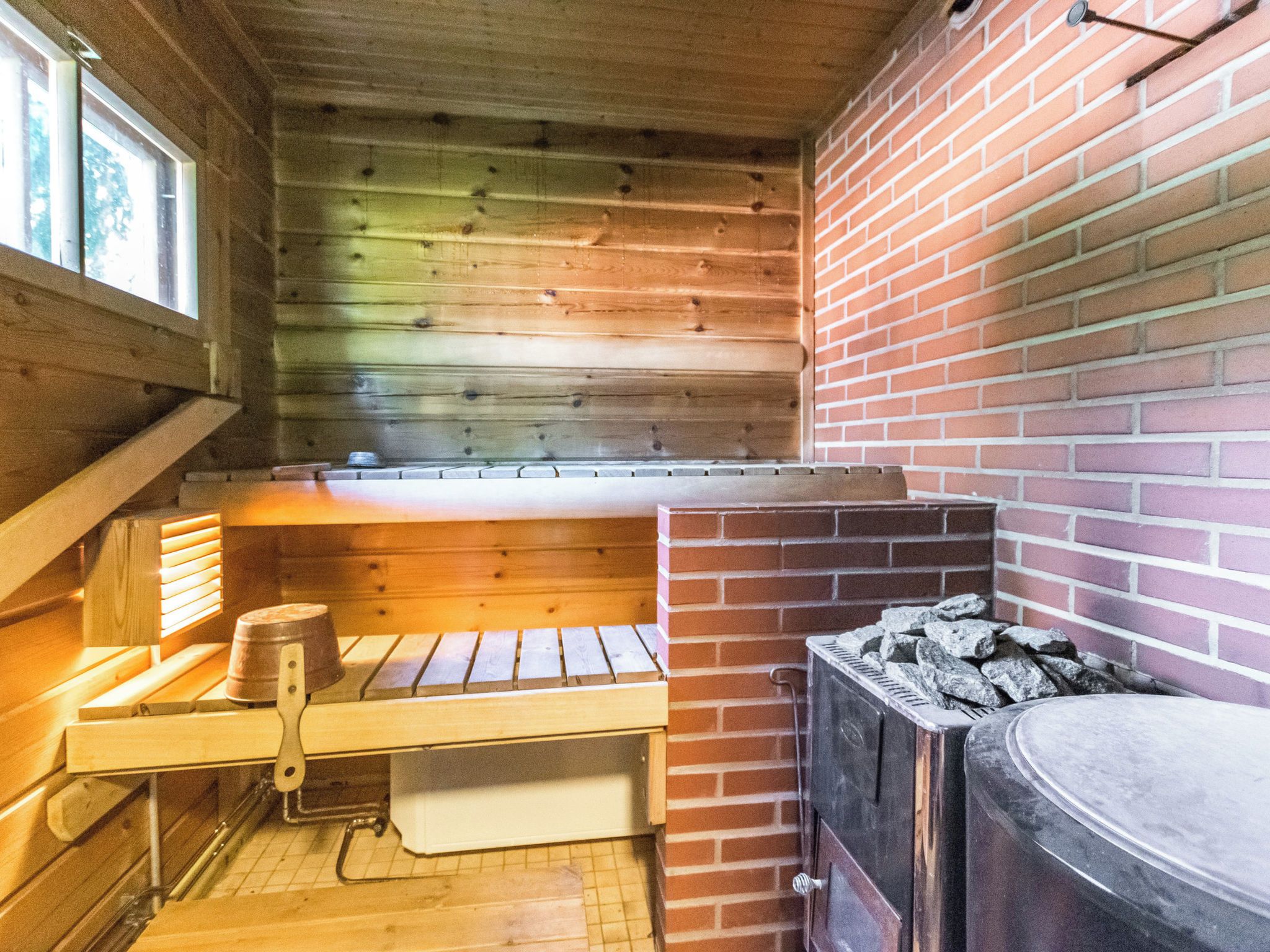 A wooden cabin interior with a brick fireplace, a wooden bench, and a window.