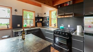 Una cocina moderna con armarios negros, un refrigerador de acero inoxidable, una estufa a gas y un amplio ventanal que proporciona luz natural.