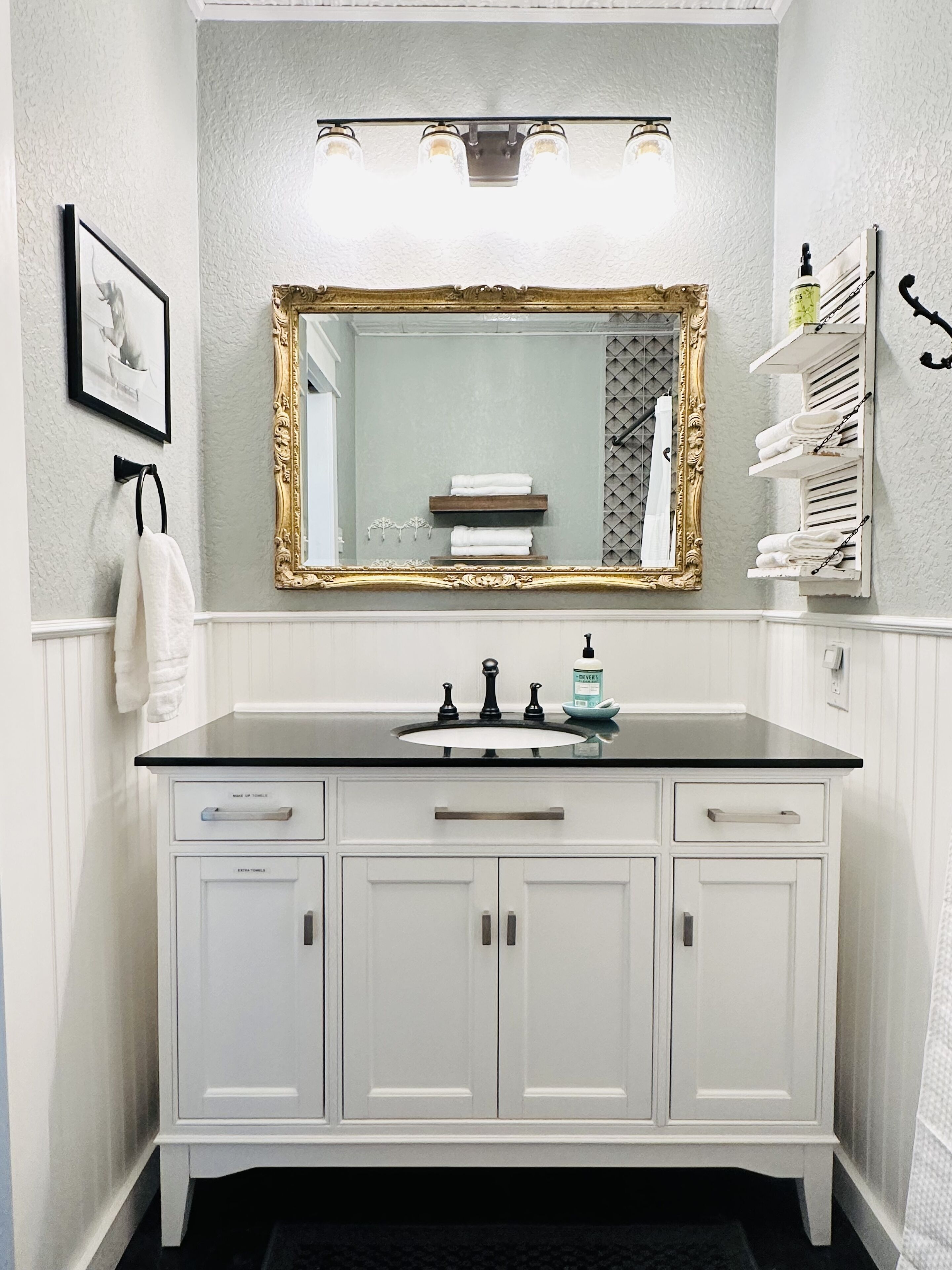 Une salle de bain avec un meuble-lavabo blanc, un miroir avec un cadre doré et un porte-serviettes.
