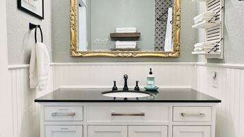 Une salle de bain avec un meuble-lavabo blanc, un miroir avec un cadre doré et un porte-serviettes.