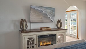 A fireplace with a fire, a painting of a beach, and a door leading to a balcony.