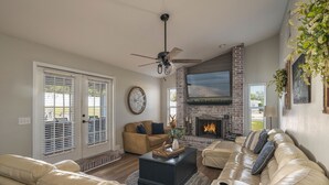 A living room with a fireplace, leather sofas, a coffee table, and a ceiling fan.