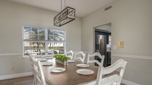 A dining room with a wooden table, white chairs, and a hanging light fixture.