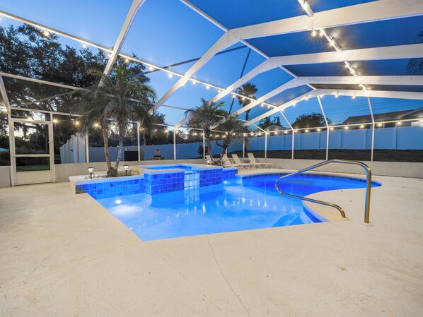 Una piscina con diseño de azulejos azules, rodeada por un porche cubierto con barandillas blancas y luces cálidas.