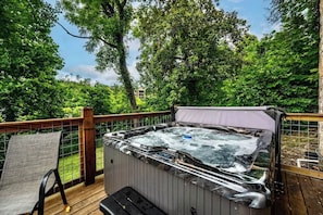 A hot tub on a wooden deck with a view of lush greenery and a building in the background.