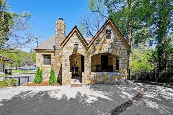A stone house with a chimney, a porch, and a fenced yard.