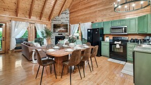 Ein geräumiger Essbereich mit einem Holztisch und Stühlen, einem Kamin aus Stein und grünen Küchenschränken.