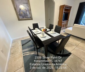 A dining area with a table set for four, a white sofa, and a wooden cabinet in the background.