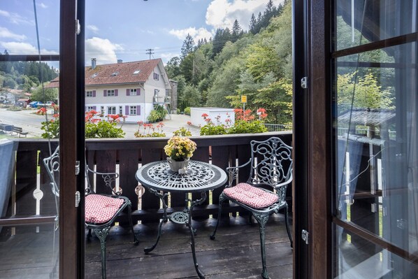 A balcony with two chairs and a table, overlooking a residential area with houses and trees.