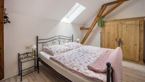 Une chambre avec un puits de lumière, un lit avec une literie à motifs floraux, une table de chevet avec une lampe et une armoire en bois.