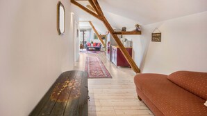 Une pièce avec un banc en bois, un canapé, un escalier et une vue sur une autre pièce où se trouvent un canapé rouge et un tapis.