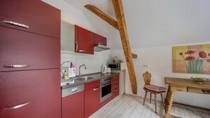 Une cuisine avec des placards rouges, une poutre en bois au plafond, un four à micro-ondes et une table à manger en bois avec une chaise.