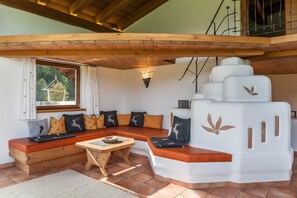 A cozy room with a wooden ceiling, a built-in bench with cushions, a small table, and a white wall with a leaf design. - Vacation Home 'Panorama Lodge Leutasch' with Mountain View, Terrace & Sauna (Leutasch)