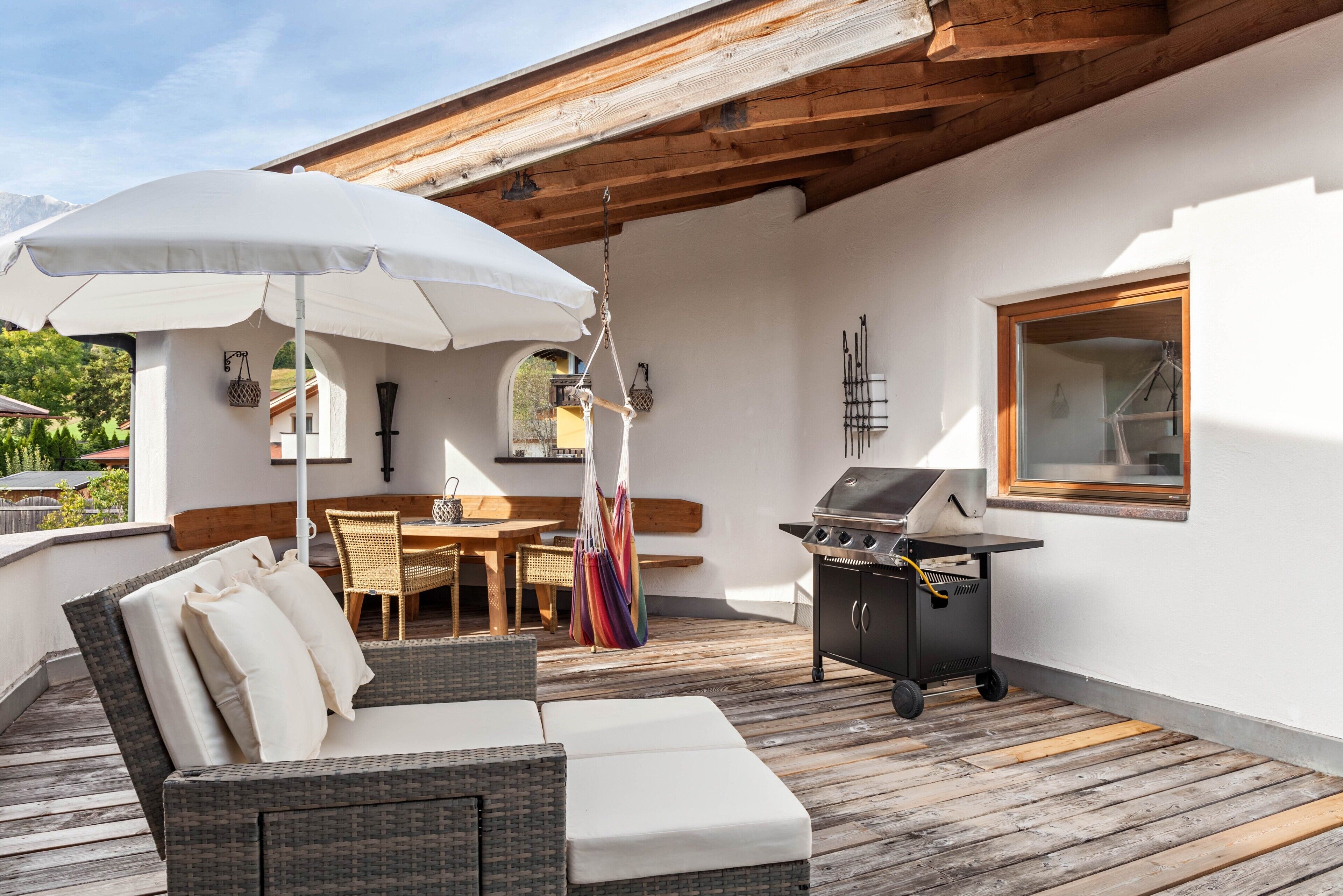 A covered outdoor area with a wicker sofa, a table, chairs, a grill, and a hanging hammock.