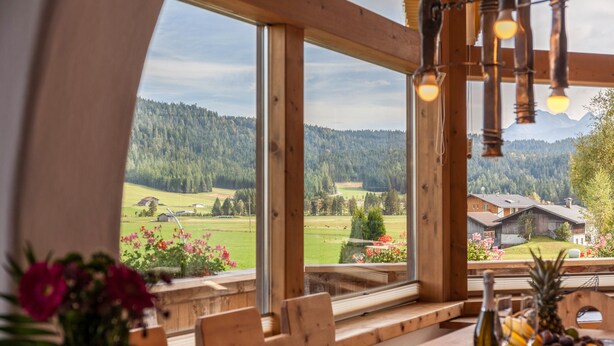 A wooden interior with large windows offering a view of a green landscape and a mountain.