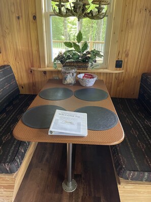 Un interior de madera con una mesa, dos sillas, un folleto de bienvenida, un tarro y un cuenco de aperitivos.