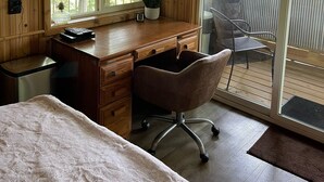 Interior de una cabaña de madera con un escritorio, una silla y ventanas amplias.