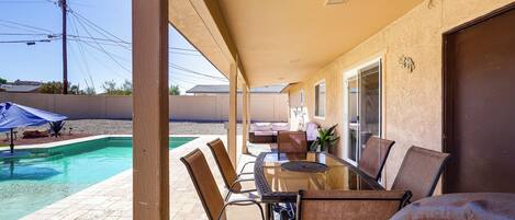Un espacio de patio techado con piscina, mobiliario exterior y vistas del vecindario.