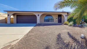 Ein Bungalow mit Garage, überdachter Auffahrt und einem begrünten Vorgarten mit Palmen.