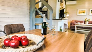 A wooden table with a bottle of champagne, two glasses, and a woven basket of red apples.