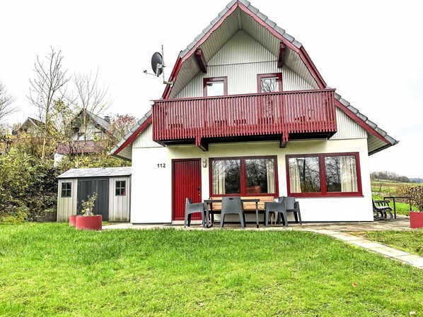 Ein zweistöckiges Haus mit einem roten Balkon, einer Sat-Schüssel und der Hausnummer 112.