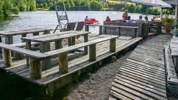 A wooden dock with benches, a small boat, and a building with an umbrella.