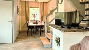 A compact living space with a dining area, a kitchen with a TV, and a staircase.
