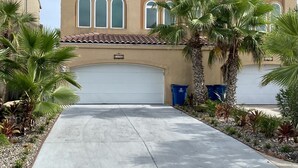 A two-story house with a garage, palm trees, and a clear sky. - Luxurious 3 Story Townhome, private pool, Elevator, 3 minute walk to the beach!! (South Padre Island)