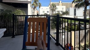 A balcony with a wooden chair, a view of palm trees, and a building in the background. - Luxurious 3 Story Townhome, private pool, Elevator, 3 minute walk to the beach!! (South Padre Island)