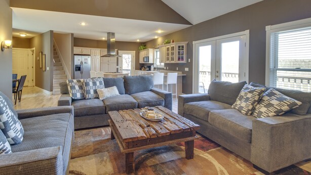 A spacious living room with a large coffee table, grey sofas, and a view of the kitchen and dining area. - Secluded Flippin Home < 2 Mi to White River! (Flippin)