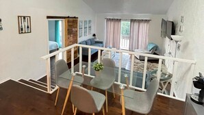 A modern dining area with a glass table and grey chairs, a wooden staircase, and a view of a balcony with a sofa and curtains. - Perfect Lake Escape (Holiday Island)