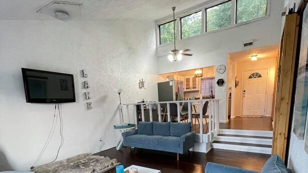 A spacious living room with a large blue sofa, a white coffee table, and a grey patterned rug. A flat-screen TV is mounted on the wall, and there is a staircase leading to an upper level. - Perfect Lake Escape (Holiday Island)