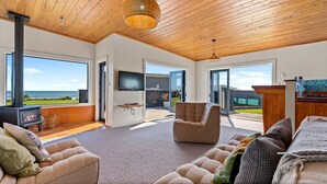 A modern living room with a fireplace, large windows, and a view of the ocean. - Coastal Daze - New Plymouth Holiday Home (New Plymouth)