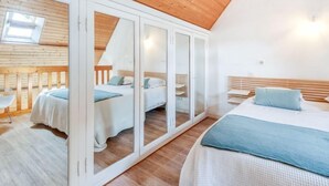 Ein Schlafzimmer mit Holzbalkendecke, Dachfenster und einem Spiegelkleiderschrank.